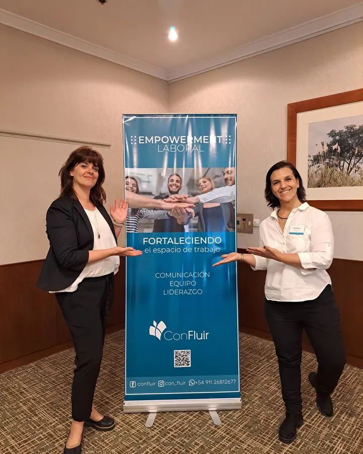 Mariana Rey y Cecilia Schifini junto al banner de Confluir «Fortaleciendo el espacio de trabajo»